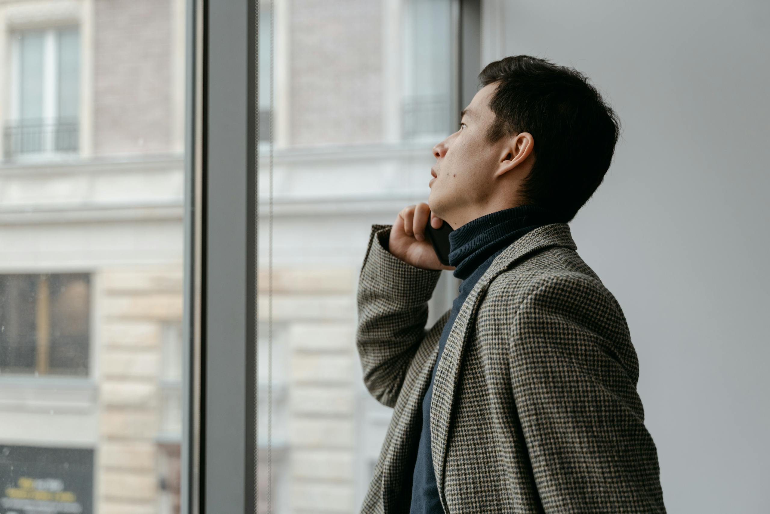 Side profile of a thoughtful businessman gazing out of a window in a contemporary office setting.
